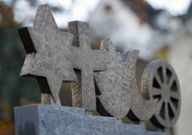 I simboli di ebraismo, cristianesimo, induismo, islam e buddismo su un monumento in un cimitero