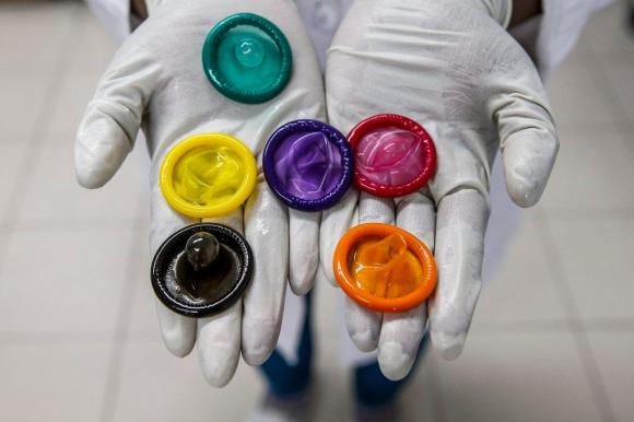 Sui palmi di due mani protette da guanti di lattice sono mostrati preservativi di vari colori.