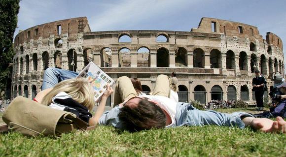In un immagine d archivio, due giovani sdraiati su un prato di fronte al Colosseo chiacchierano sfogliando una guida di Roma.