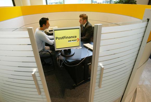 Un consulente finanziario di Postfinance discute con un cliente attorno a un tavolo.