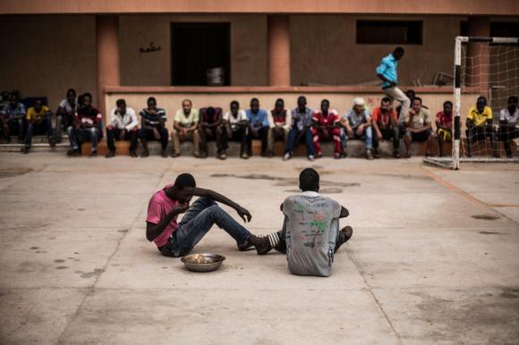 due migranti seduti per terra in un centro di detenzione libico