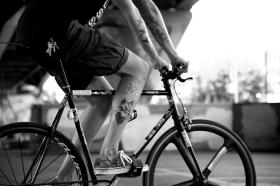 Una persona, di cui non si vede il viso, ma solo le braccia e le gambe tatuate, in sella a una bici.