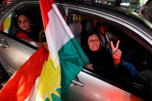 Anziana signora fa il gesto della vittoria mentre regge una bandiera curda.