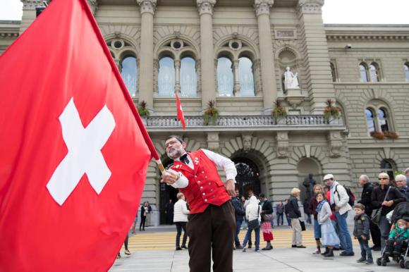 Uno sbandieratore fa volteggiare la bandiera svizzera davanti al Palazzo federale.