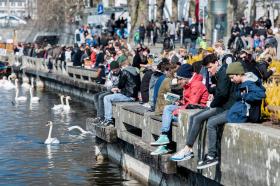 Molti giovani seduti sulle rive del Lago di Zurigo, mentre osservano dei cigni.