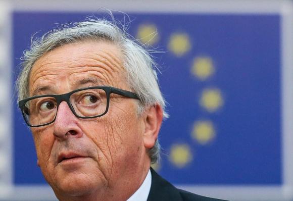 Primo piano del volto di Jean-Claude Juncker e sullo sfondo la bandiera europea.