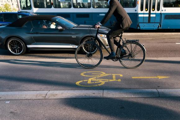 In un immagine d archivio, un ciclista sfreccia su una pista ciclabile di Zurigo passando accanto a un auto e un tram.
