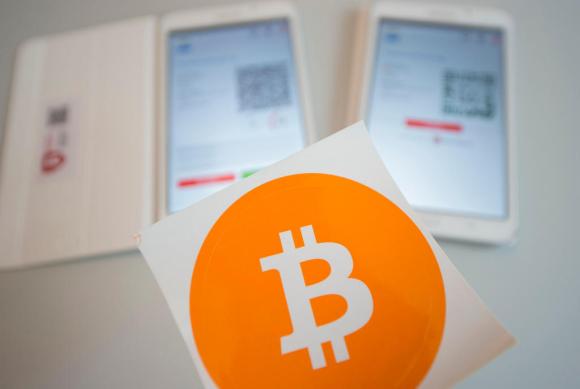 Logo del bitcoin e, sullo sfondo, due tablet pronti per una transazione in criptovaluta a uno sportello comunale di Zugo