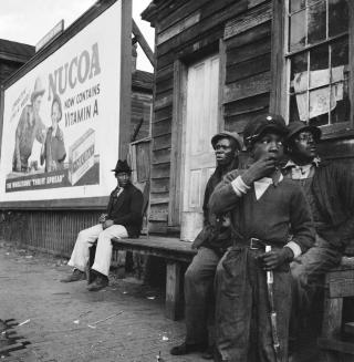 Eine Gruppe von Afroamerikanern sitzt vor einem Holzhaus