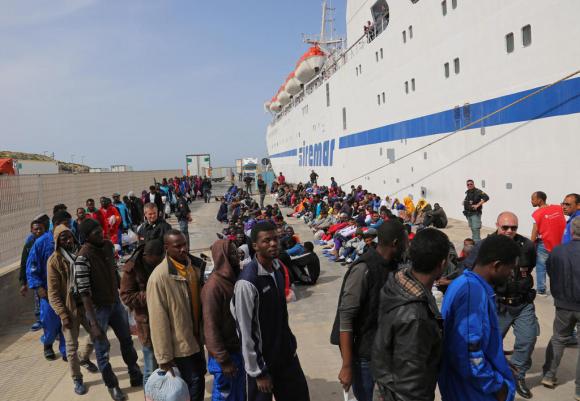 fila di migranti in attesa di imbarcarsi su una nave a Lampedusa