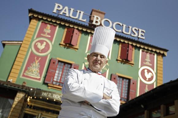 Lo chef Paul Bocuse ritratto davanti al suo ristorante. Sul tetto dell edificio, una grande insegna riporta il suo nome.