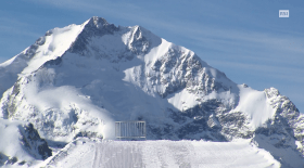 Una ringhiera semicircolare in mezzo alla neve e il pizzo Bernina sullo sfondo.