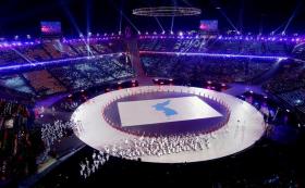 Un anello illuminato di bianco al centro di uno stadio sul quale sfila la delegazione di atleti coreani.