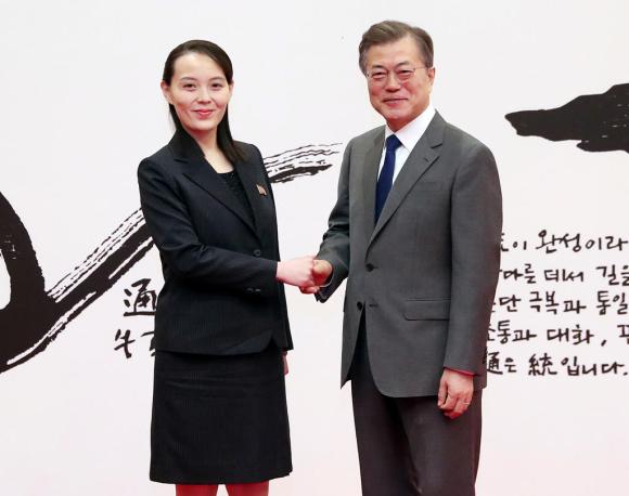 Kim Yo-jong e Moon Jae-in si stringono la mano. Sullo sfondo, un illustrazione con caratteri coreani