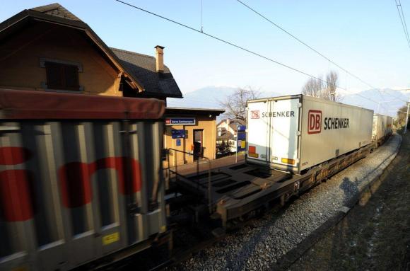 Un treno merci passa in una piccola stazione lungo il Lago Maggiore al tramonto