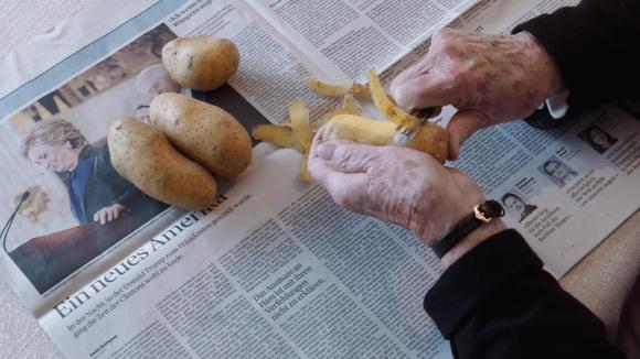 Eine ältere Frau schält über einer Zeitung Kartoffeln