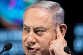 Primissimo piano di Netanyahu con un dito appoggiato alla tempia e due microfoni davanti