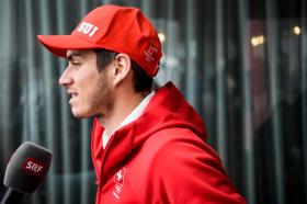 Ritratto di profilo di Elias Ambühl, che indossa tuta e cappellino rossi di Swiss Ski e parla in un microfono di SRF
