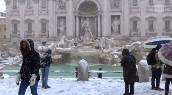 Alcune persone con abiti pesanti e ombrelli davanti alla Fontana di Trevi, mentre nevica.