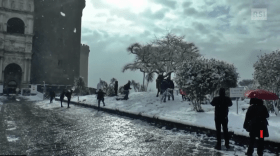 Immagine scattata nei pressi del Maschio Angioino a Napoli. Alberi e prato innevati. Cielo scuro. Gente che gioca con la neve.