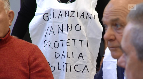 Durante una manifestazione un anziano indossa mantellina con la scritta gli anziani vanno protetti dalla politica
