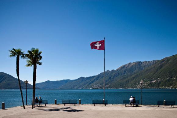 due palme, una bandiera svizzera al vento e alcune panchine in riva a un lago