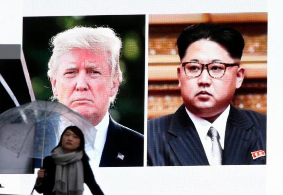 Schermo con volto di Trump e Kim, donna con ombrello
