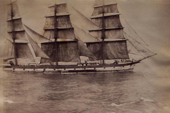 An old photo of a ship full sail at sea.