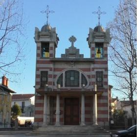 Facciata di una chiesa stile liberty con due guglie e rosone, albero spoglio a destra.