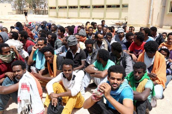 Un gruppo di uomini africani seduti per terra in un centro di detenzione di migranti clandestini in Libia.