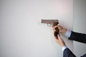 Un uomo impugna una pistola e inserisce il caricatore, sul fondo solo un pannello bianco