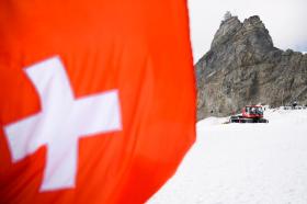 Bandiera svizzera sfocata in primo piano, montagna (Jungfraujoch) e gatto delle nevi a fuoco in lontananza