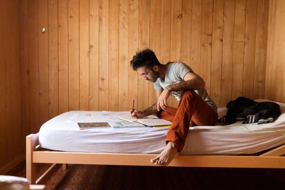 Un uomo siede su un letto e prende appunti in un quaderno