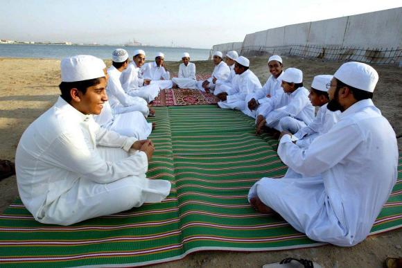 gruppo di ragazzi arabi vestiti con il tradizionale abito bianco seduti su un tappeto sul fronte mare di Jeddah