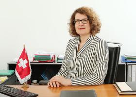 Rita Adam seduta alla scrivania, sulla quale c è una bandiera svizzera. 