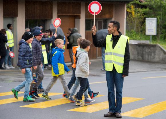 Richiedenti l asilo aiutano degli scolari ad attraversare la strada.