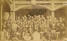 Foto di gruppo ottocentesca, ingiallita; sul fondo un portico sovrastato da uno scudo rossocrociato