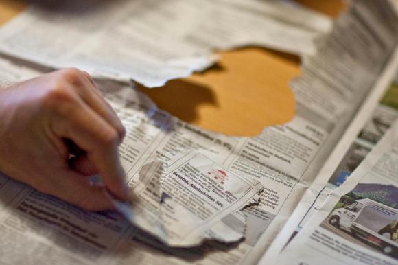 Pagina di giornale con annunci di lavoro, una mano ne tiene uno (strappato dal foglio) tra pollice e indice