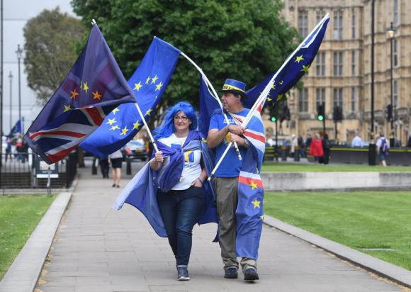 Un uomo e una donna camminano davanti al parlamento inglese con bandiere europee e britanniche