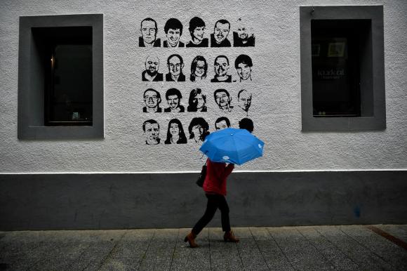 donna con un ombrello davanti a un muro con dei ritratti di prigionieri dell eta