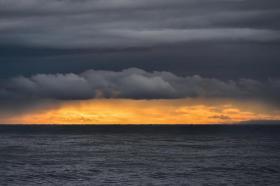 Immagine del mare al tramonto, sovrastato da nubi scure