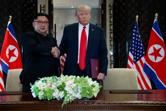 La stretta di mano tra Kim Jong-un e Donald Trump tra le bandiere dei due paesi