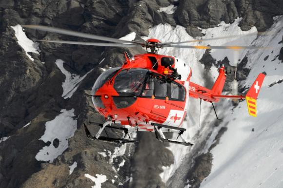 elicottero della Rega in volo davanti a una montagna