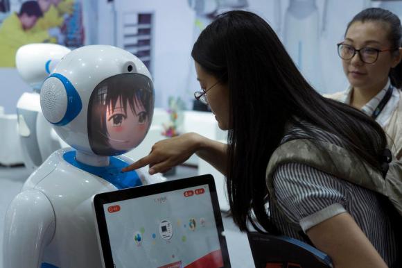 Una donna interagisce con un robot cinese: la tecnologia sarà uno dei settori toccati dai dazi che gli USA impongono alla Cina