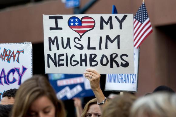 Durante una manifestazione di protesta, un donna solleva un cartello con scritto Amo i miei vicini musulmani