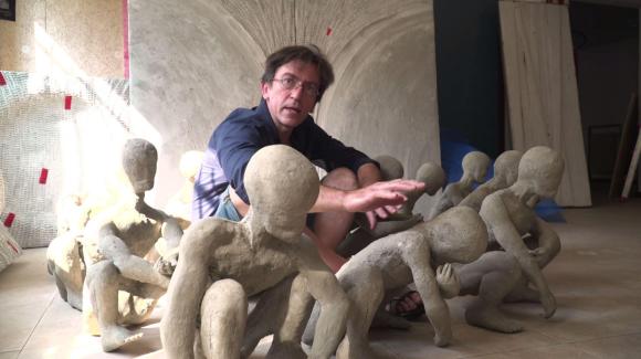 L artista Daniele Pigoni accovacciato e attorniato dalle sue sculture
