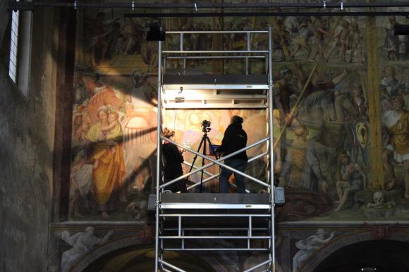 Immagine di un grande dipinto murale con due persone su un impalcature che lo osservano con l aiuto di un faretto