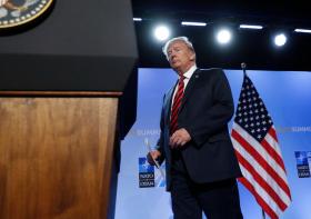 Il presidente americano si avvicina a un pulpito; sullo sfondo il logo NATO-OTAN e una bandiera USA