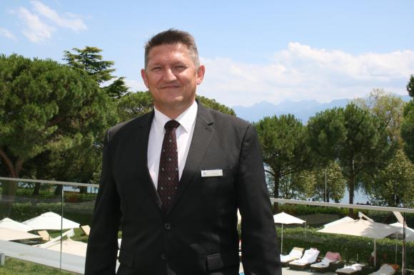 Stéphane Garnier in completo giacca e cravatta posa nel parco del grande albergo dove lavora.