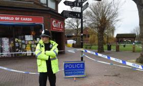 Agente di polizia britannica con mantellina catarifrangente in piedi davanti a un negozio e una zona sbarrata